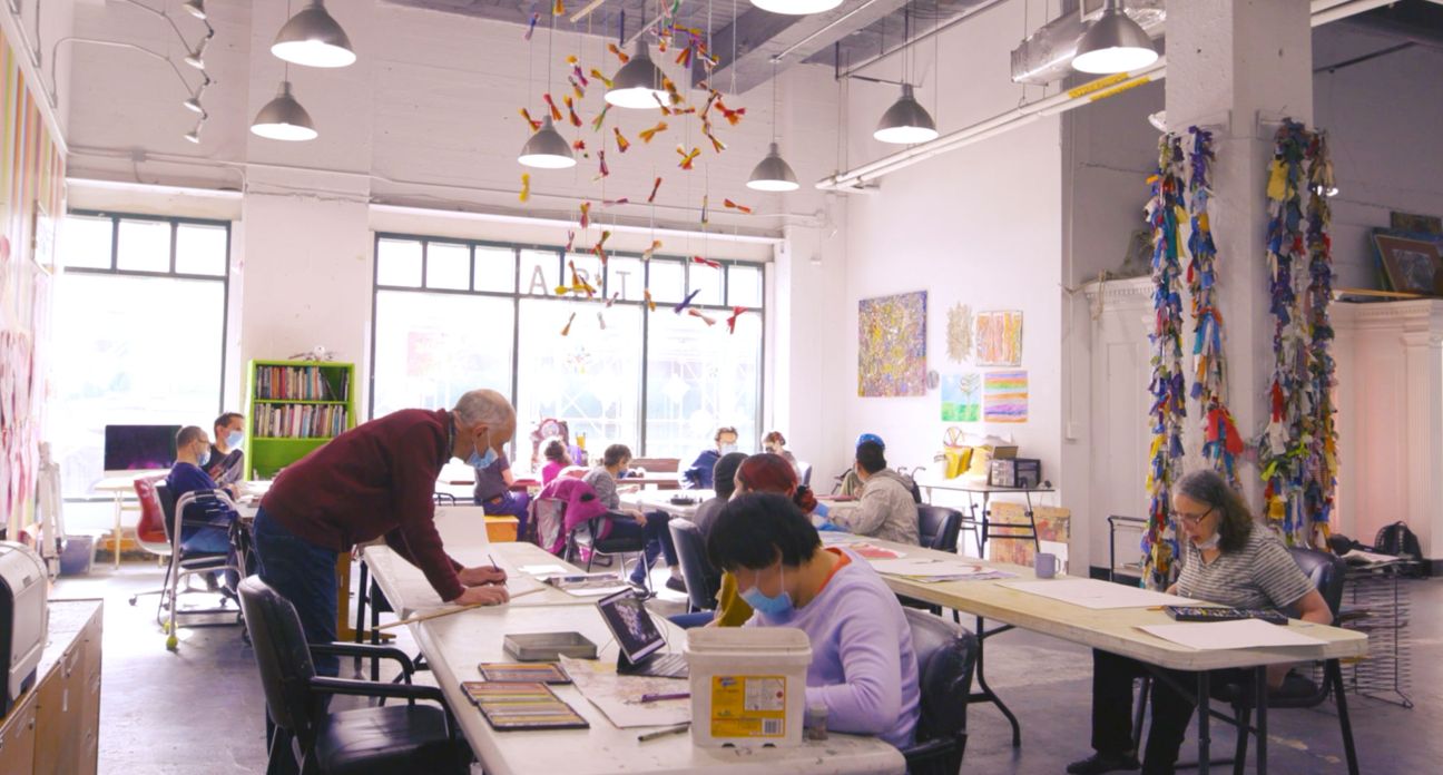 People creating artwork at the Maggie Daly Arts Cooperative with art hanging from the ceiling.